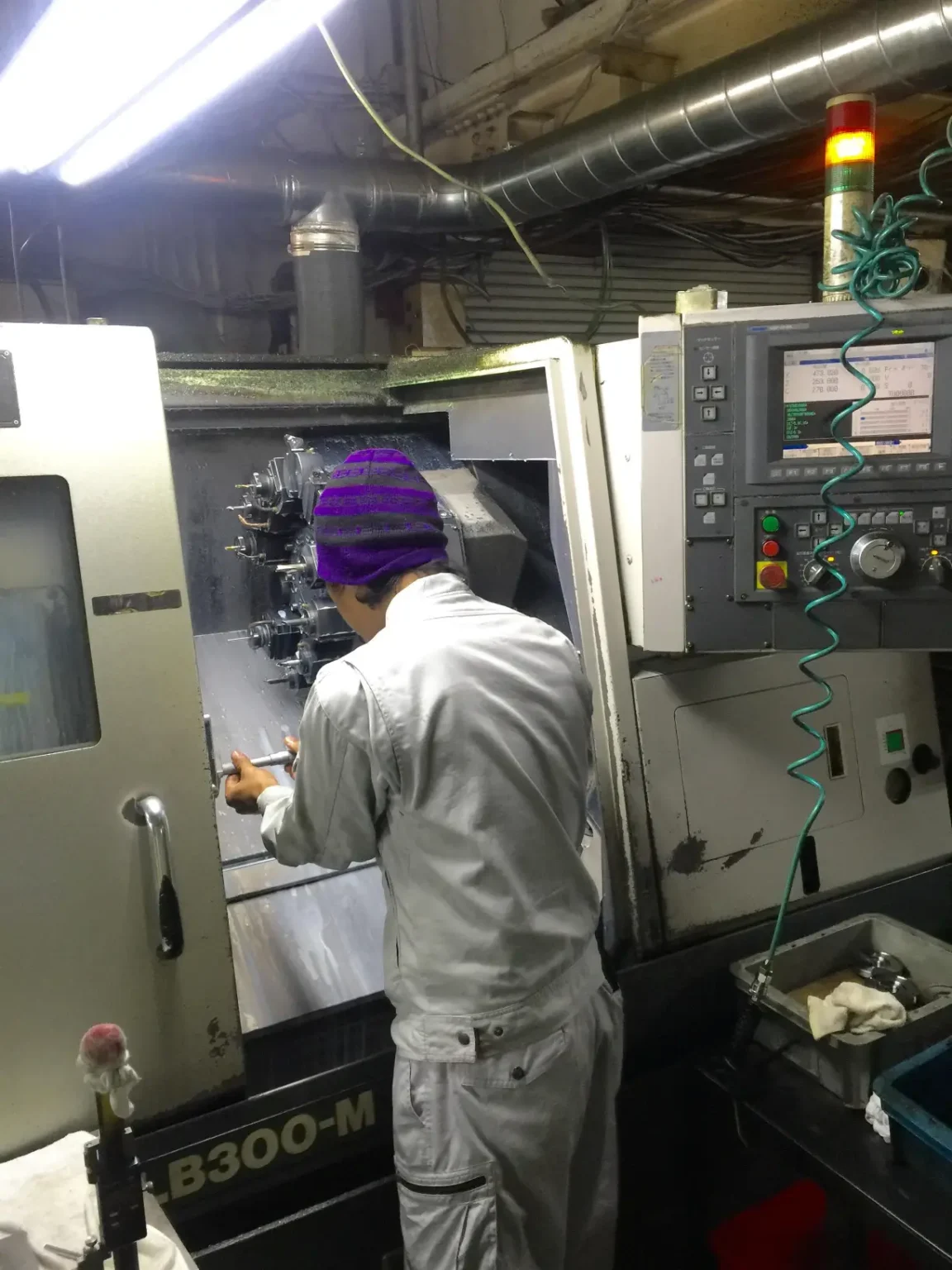 A technician in a white jumpsuit operates a CNC machine in a workshop.