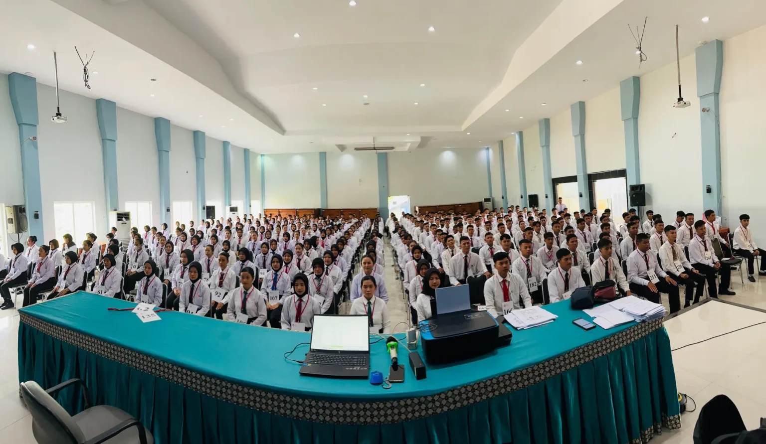 A crowded auditorium filled with seated students in white shirts and ties.