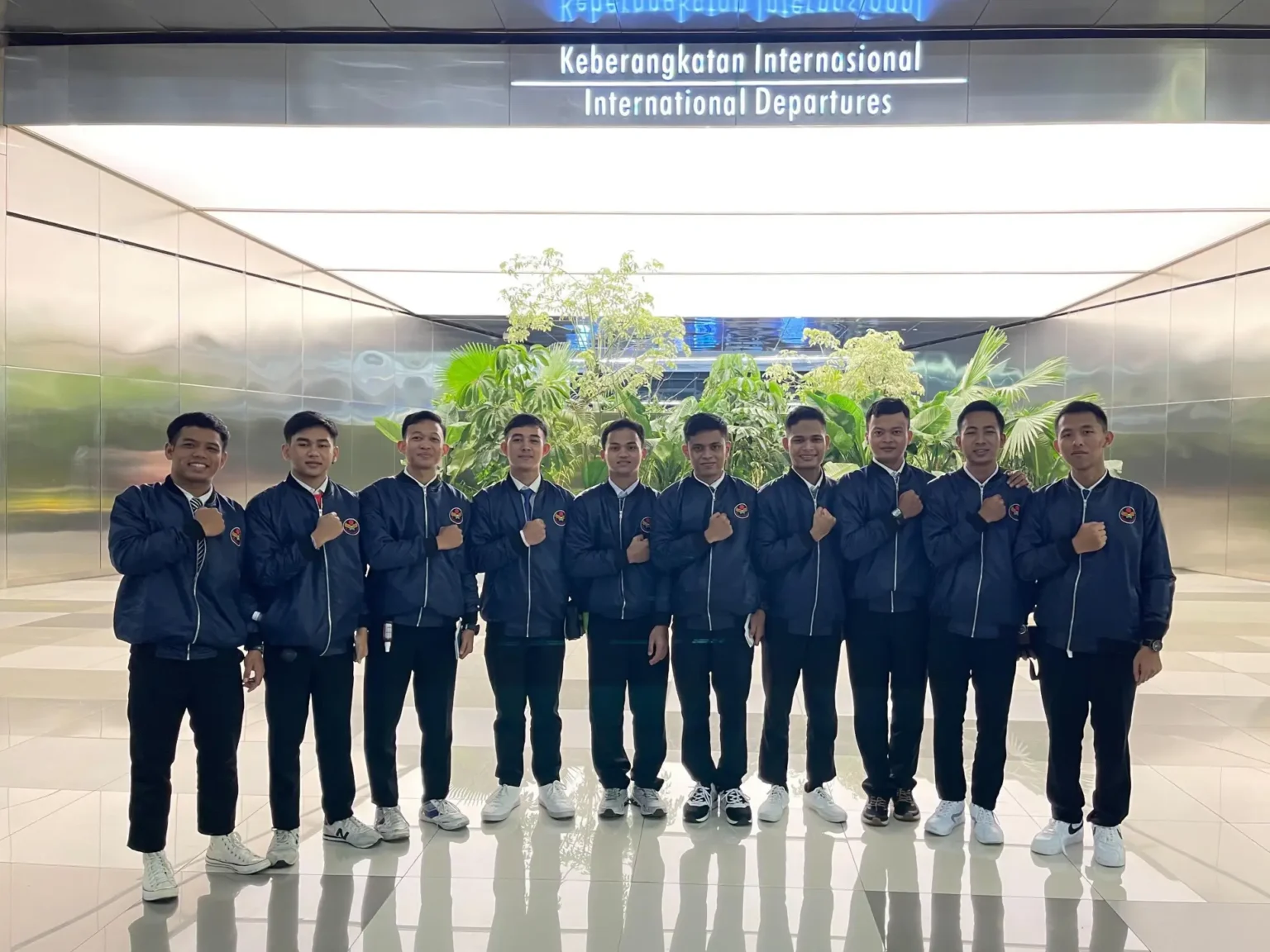 A group of ten individuals in matching navy jackets stands in a modern airport terminal.