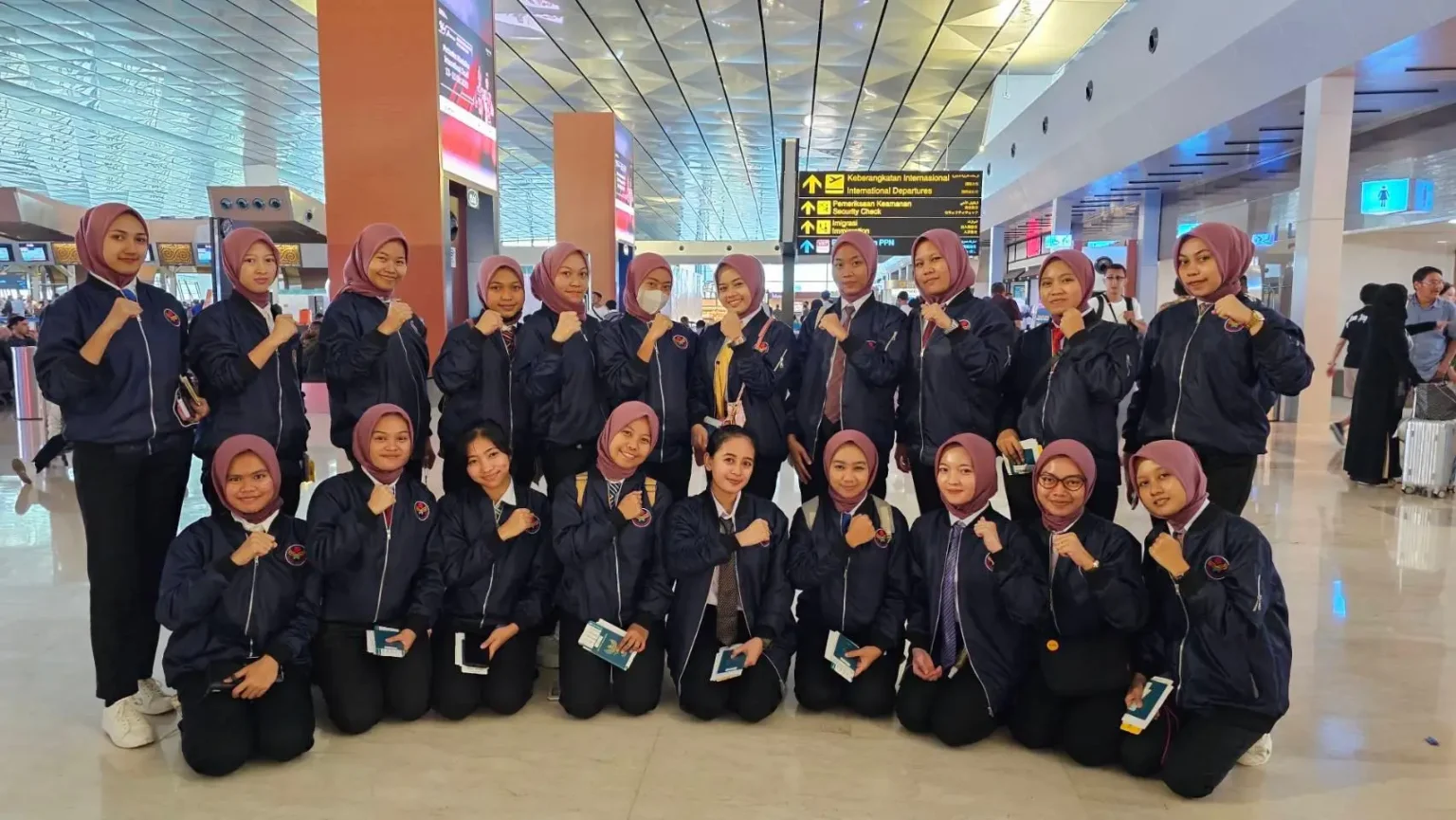 A group of young individuals in matching jackets and headscarves pose together in an airport